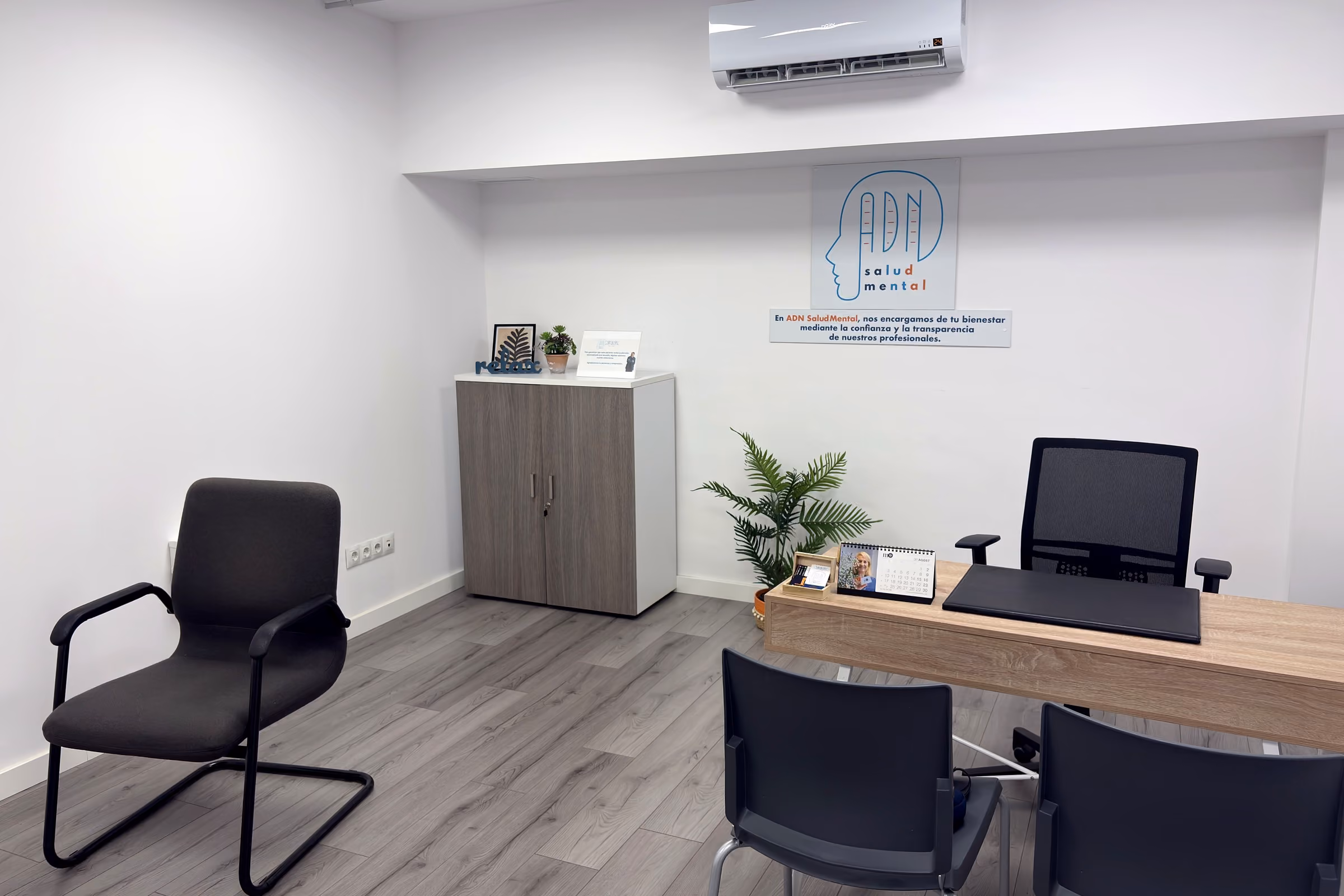 La sala vista desde la puerta: una butaca junto a la pared, un armario y la mesa de trabajo al fondo.